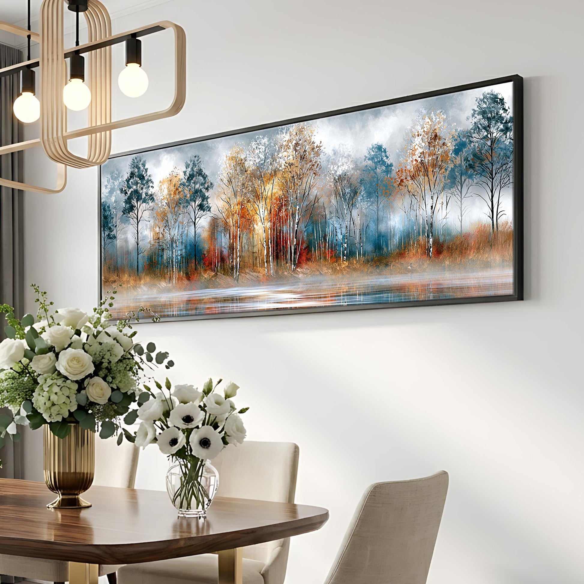 a dining room with a large painting of a forest scene hanging on the wall above a wooden table. The table is set with a vase of white flowers and a potted plant. The room has a modern and elegant design, with a chandelier and a white wall.
