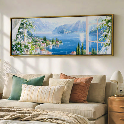 a large, framed painting of a scenic landscape with a river, mountains, and a town, hanging on a wall above a beige sofa with decorative pillows.